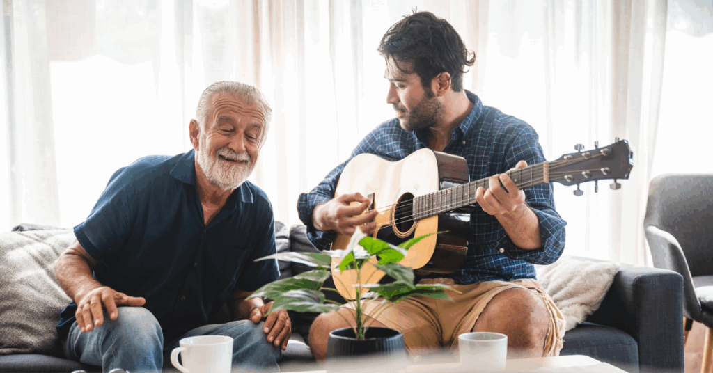 A male music therapist playing guitar with an older man.