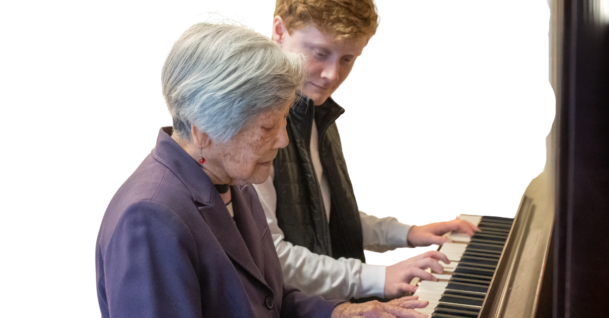 Male music therapist playing the piano with an elderly woman.