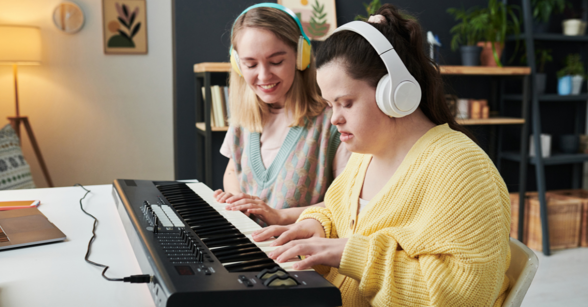 A music therapist and a young woman sitting at a piano keyboard.