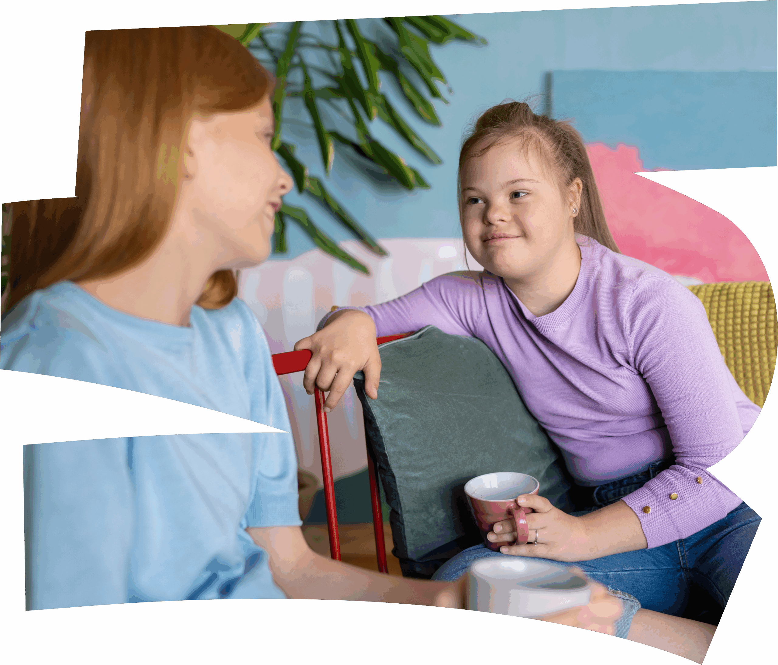 Two young women sit together indoors, smiling and talking while holding mugs. One woman has Down syndrome and wears a purple top; the other, in a light blue shirt, discusses music therapy courses. Green plants are visible in the background.