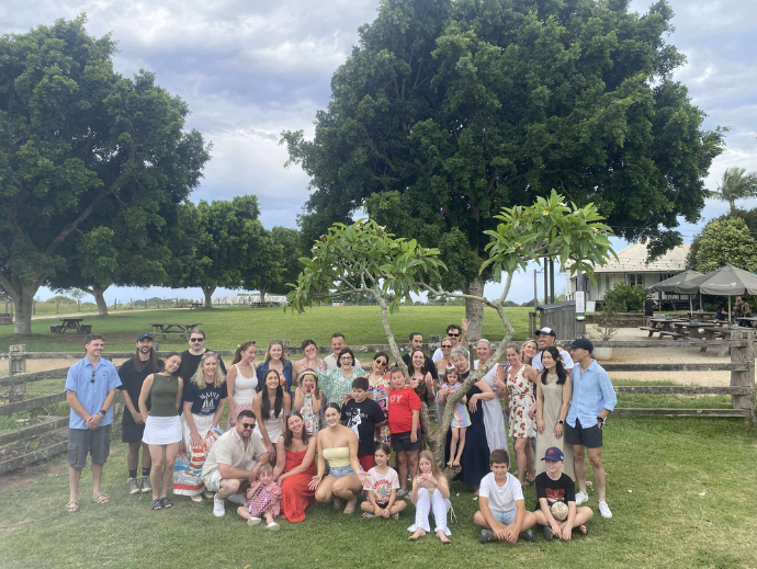 A group photo of 40 adults and children on a farm with large trees in the background.