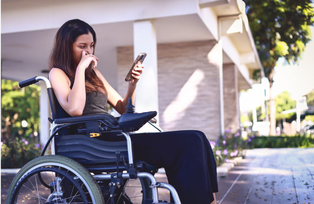 A woman sitting in a wheelchair looking at her mobile phone with a concerned look.